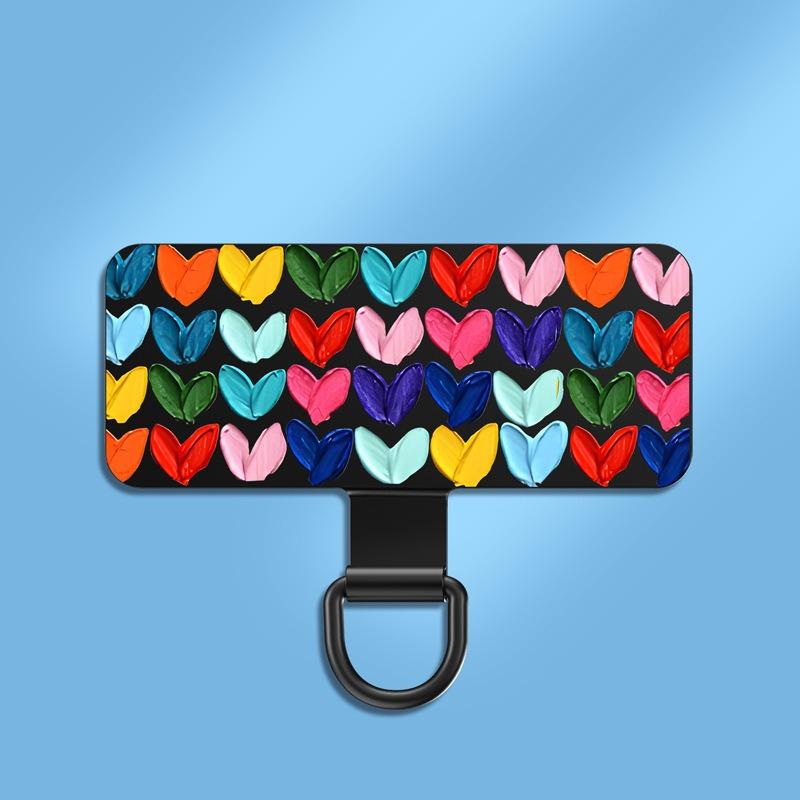 Y143 ultra-thin stainless steel phone tether tab covered in a multicoloured heart print on a black plate