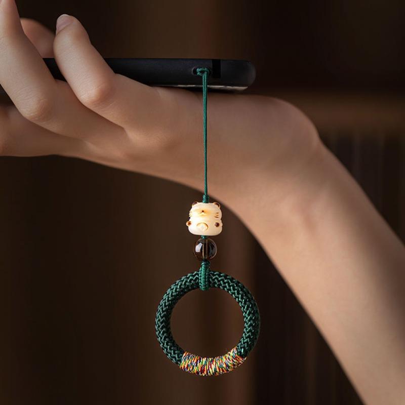 Y290 dark green ring strap worn on a finger holding a phone, showing the carved lucky cat bead and woven ring